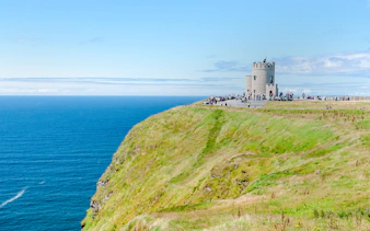 O'Brien's Tower overlooking the Cliffs of Moher, Ireland, with visitors nearby.
