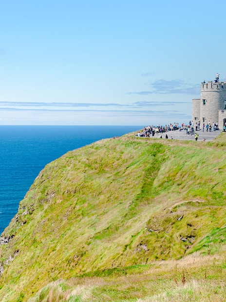 O'Brien's Tower overlooking the Cliffs of Moher, Ireland, with visitors nearby.