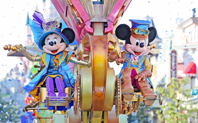Mickey and Minnie Mouse in colorful costumes on a parade float at Disneyland Paris.