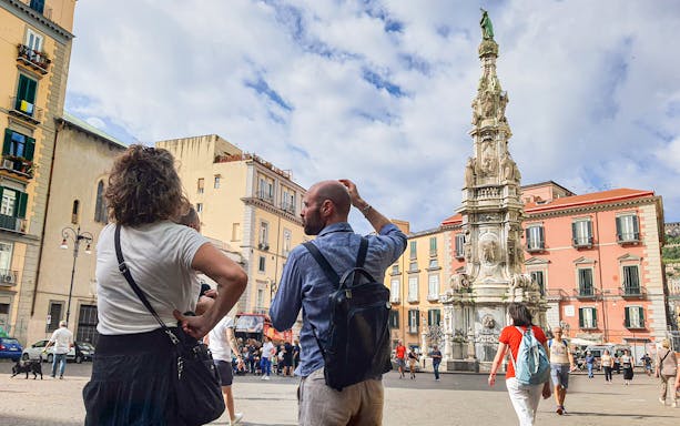 Tourists exploring Piazza del Gesù Nuovo in Naples with the Spire of the Immaculate Virgin in view.