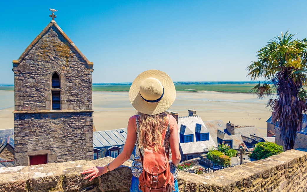 Woman overlooking Mont Saint Michel landscape with stone buildings and sandy bay.
