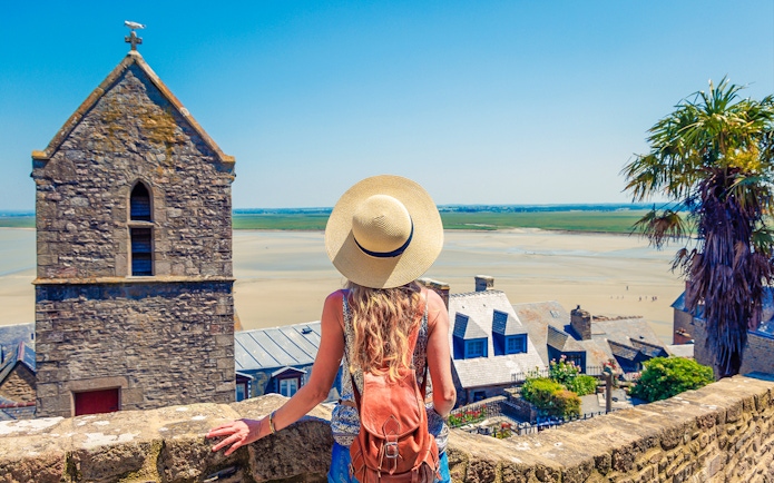Woman overlooking Mont Saint Michel landscape with stone buildings and sandy bay.