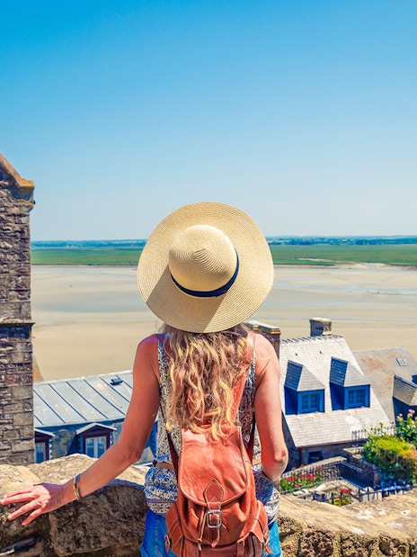 Woman overlooking Mont Saint Michel landscape with stone buildings and sandy bay.