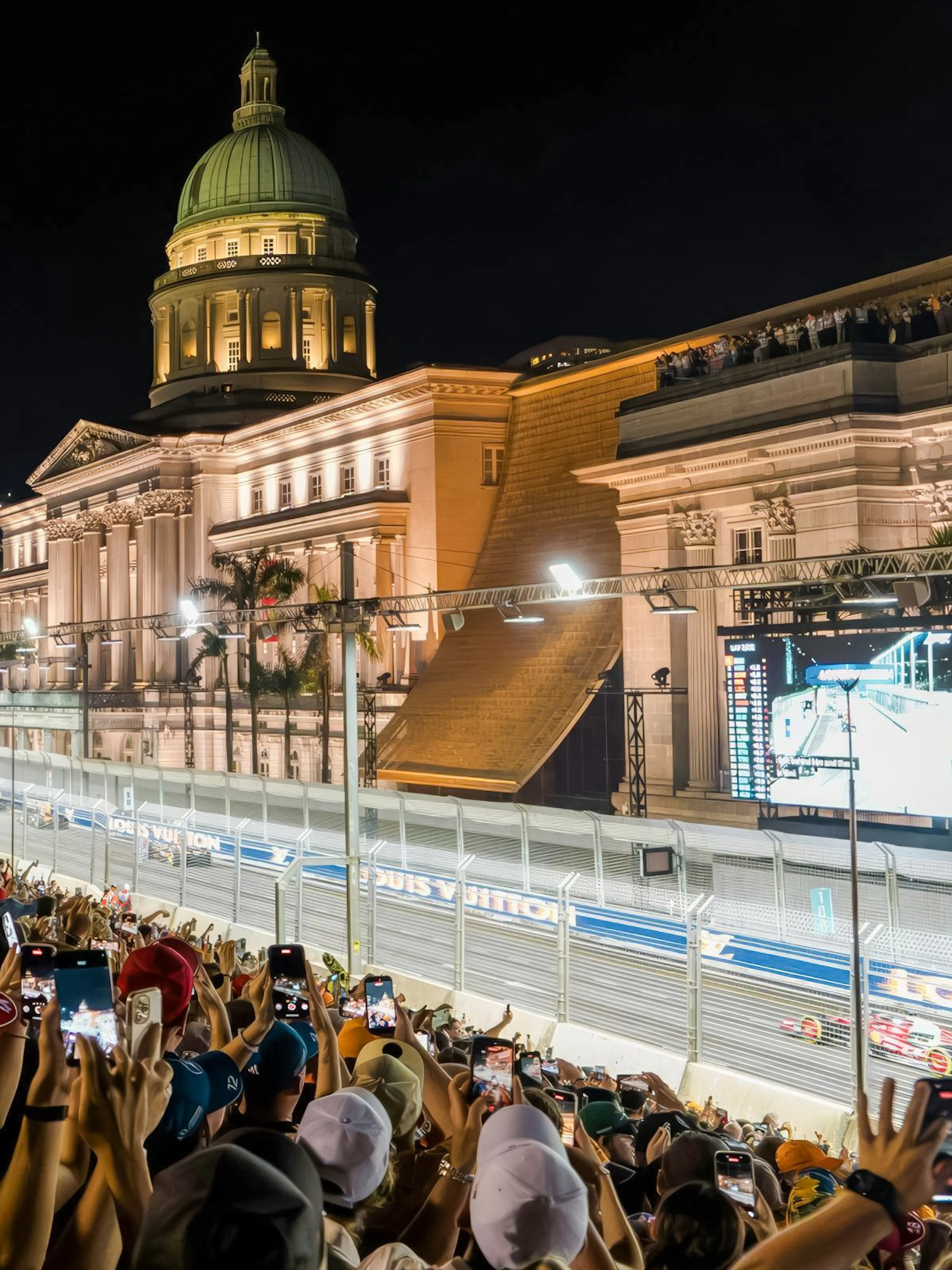 Crowd watching Formula 1 Singapore Grand Prix at Marina Bay Street Circuit with National Gallery Singapore in view.