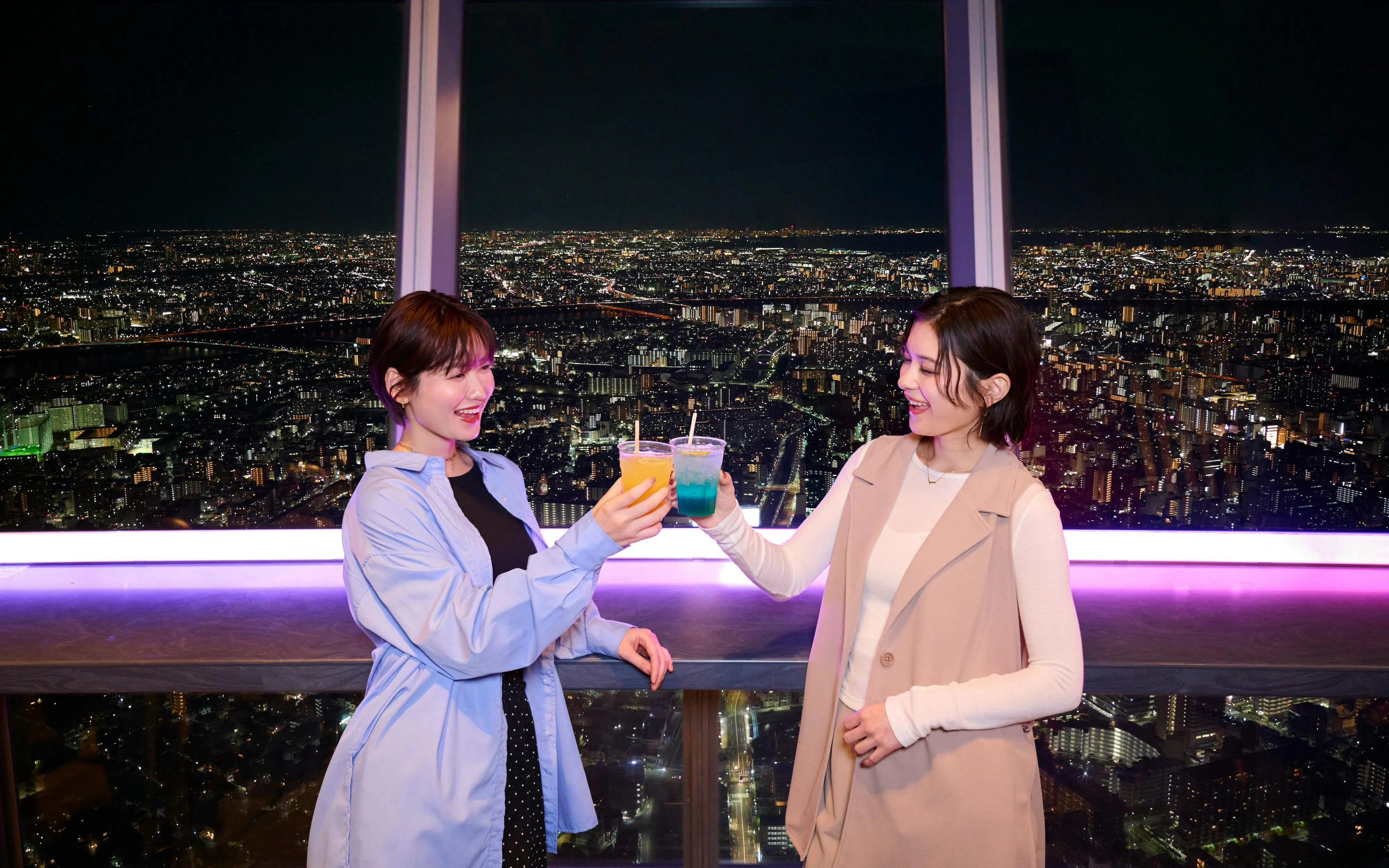 Two people enjoying drinks with a night view from Tokyo Skytree Tembo Deck.