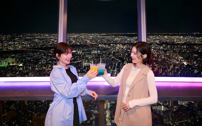 Two people enjoying drinks with a night view from Tokyo Skytree Tembo Deck.