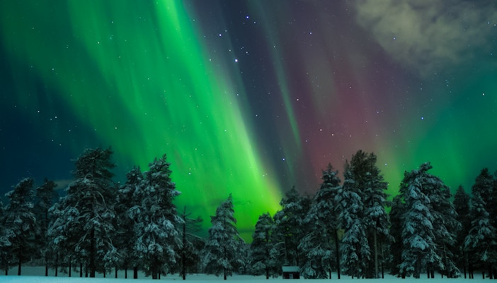 Northern Lights over snowy landscape with red cabin in Levi, Finland.
