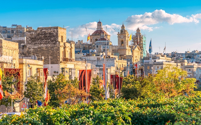 Historic buildings and clock tower in the Three Fortified Cities, Malta, with colorful banners.