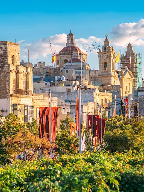 Historic buildings and clock tower in the Three Fortified Cities, Malta, with colorful banners.