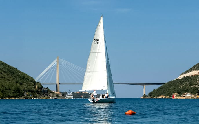 Yacht sailing near Dubrovnik with Franjo Tuđman Bridge in the background.