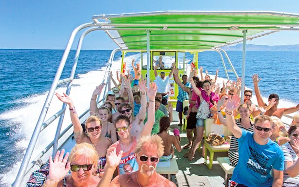 Group enjoying a boat trip in Alcudia, waving and smiling on deck.