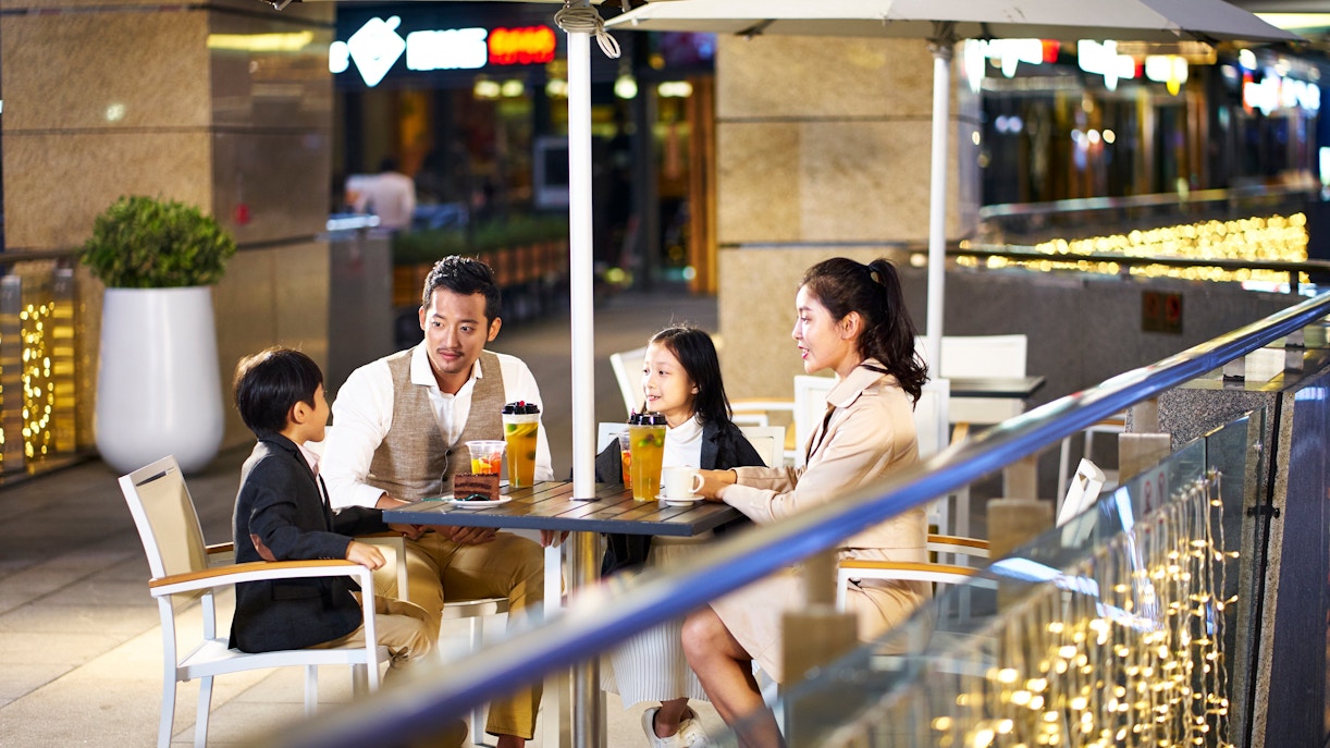 Asian family enjoying drinks at an outdoor coffee shop in a city setting.