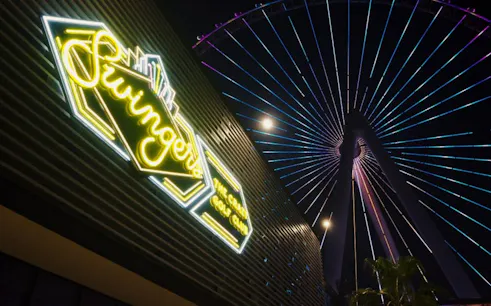 Swingers neon sign with illuminated Ferris wheel at night.