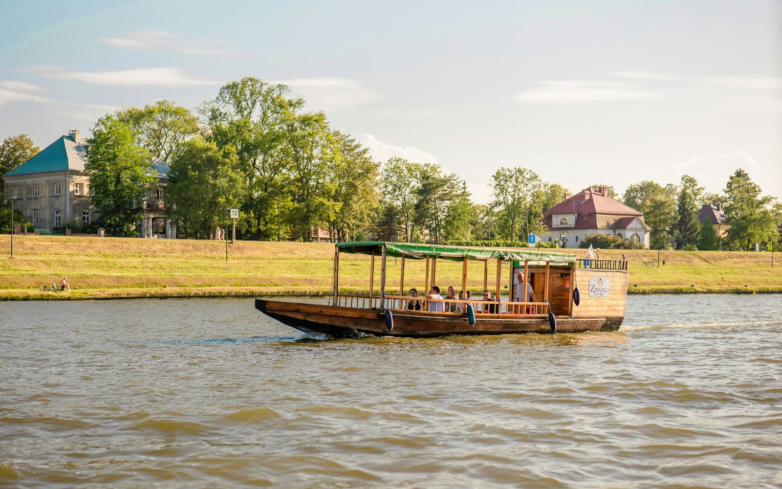 Wooden boat cruising on Vistula River with passengers enjoying the view, Krakow, Poland.