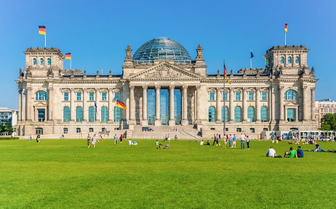 Reichstag Building in Berlin with people on the lawn, German flags flying.