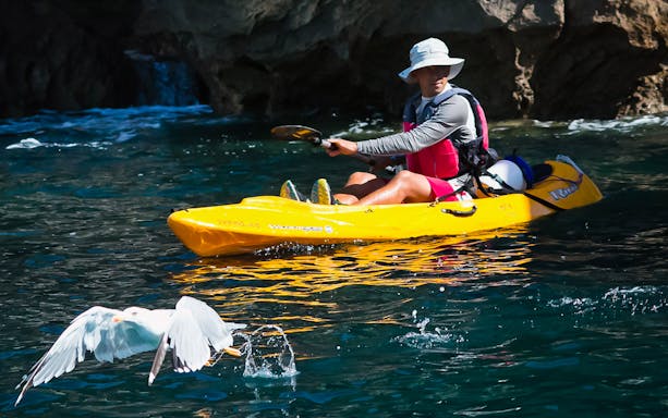 Kayakers paddling in clear waters of Arrábida Natural Park, Lisbon, with rocky cliffs in the background.