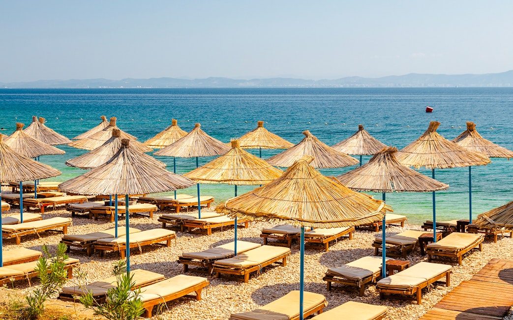 Sun loungers and straw umbrellas on Karaburun Peninsula beach, Albania.