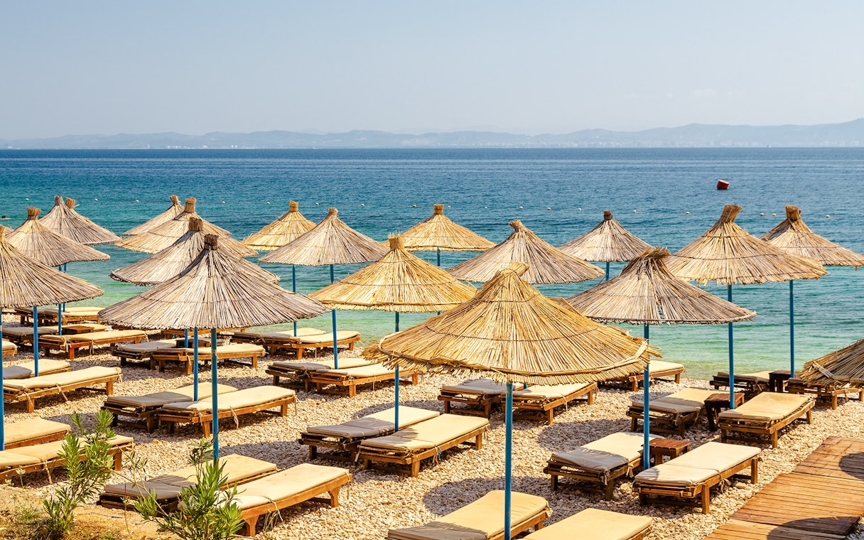 Sun loungers and straw umbrellas on Karaburun Peninsula beach, Albania.