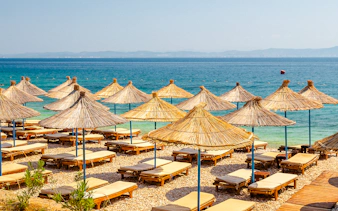 Sun loungers and straw umbrellas on Karaburun Peninsula beach, Albania.
