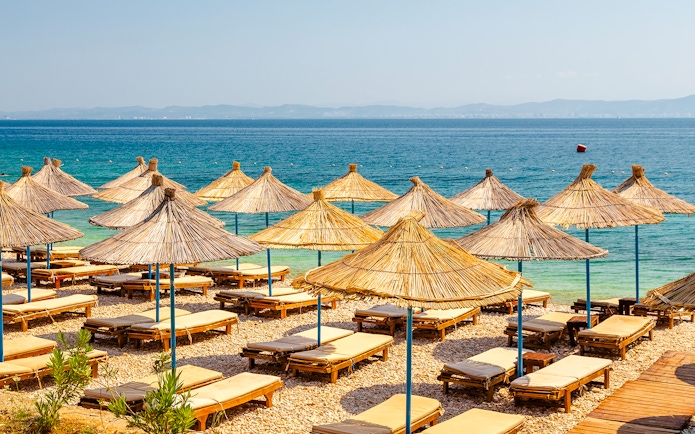 Sun loungers and straw umbrellas on Karaburun Peninsula beach, Albania.