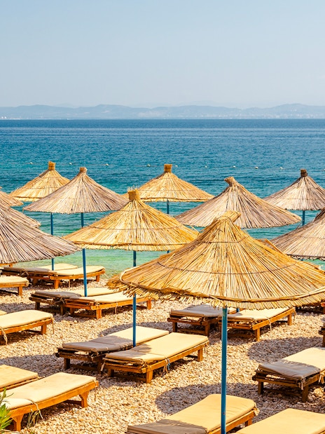 Sun loungers and straw umbrellas on Karaburun Peninsula beach, Albania.