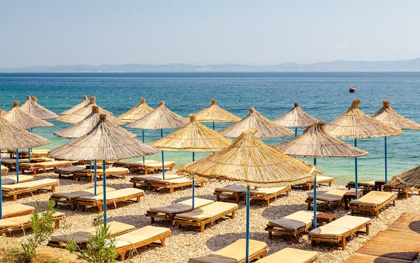 Sun loungers and straw umbrellas on Karaburun Peninsula beach, Albania.