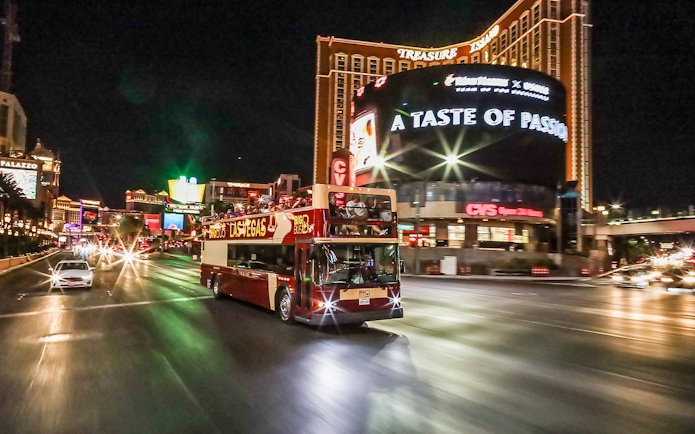 Big Bus tour driving on Las Vegas Strip at night near Treasure Island.