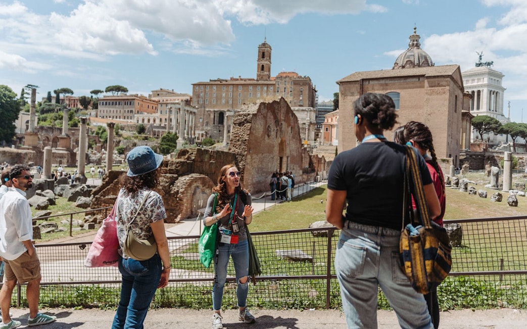 Tour guide with group at Palatine Hill, Rome, with ancient ruins in the background.