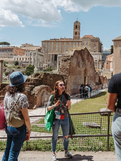 Tour guide with group at Palatine Hill, Rome, with ancient ruins in the background.