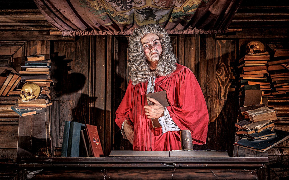 Judge in red robe at London Dungeon courtroom with books and skulls.