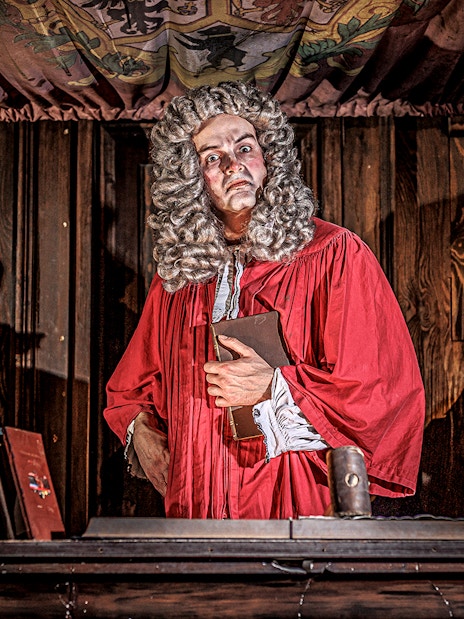 Judge in red robe at London Dungeon courtroom with books and skulls.