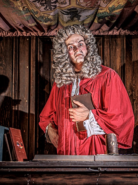 Judge in red robe at London Dungeon courtroom with books and skulls.