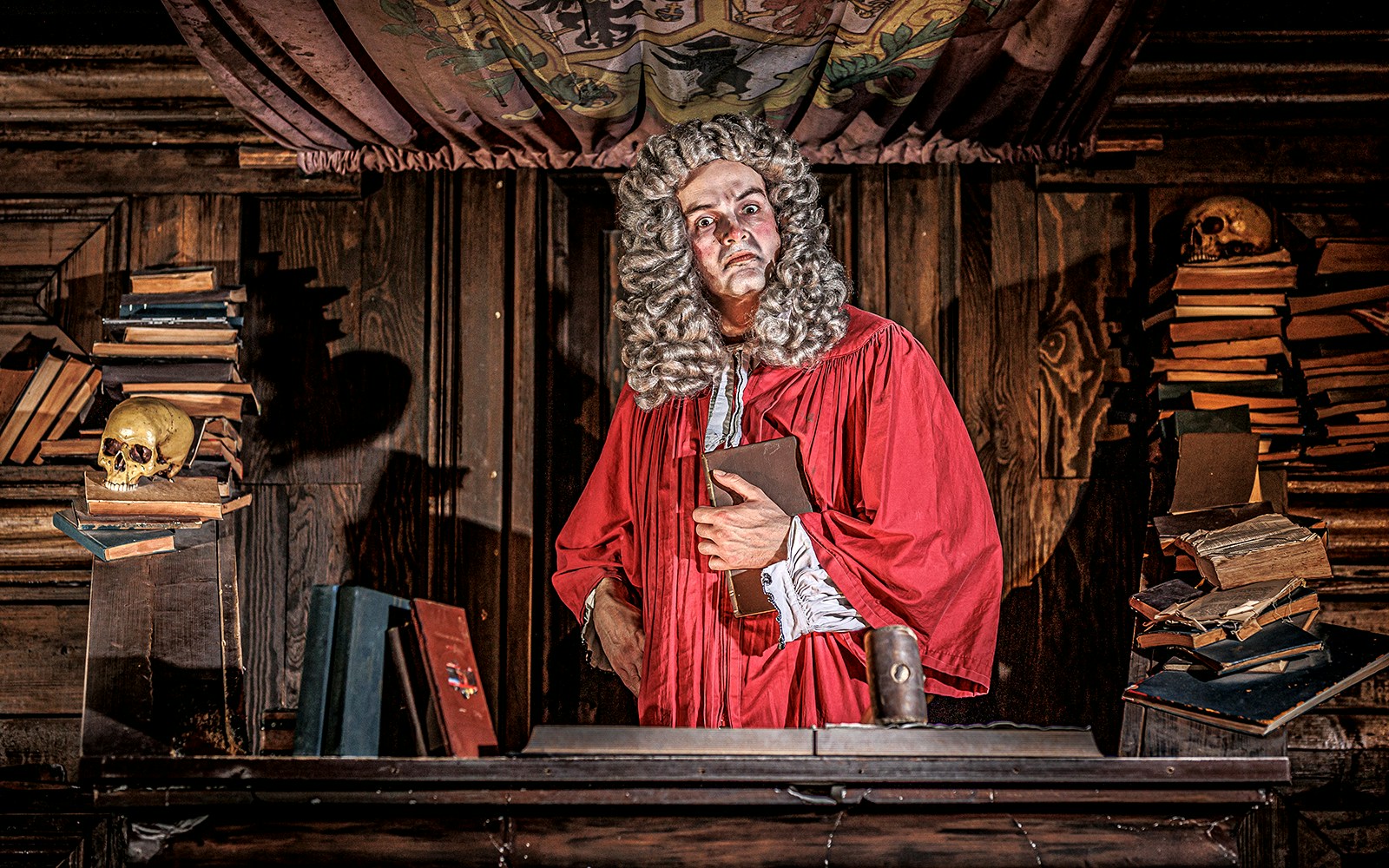 Judge in red robe at London Dungeon courtroom with books and skulls.