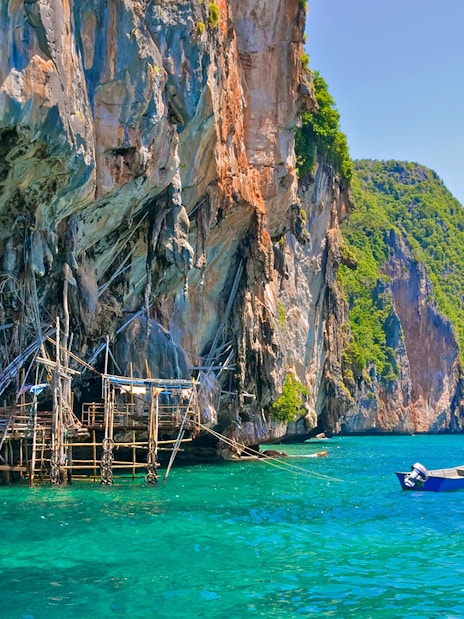 Viking Cave with wooden scaffolding and boat in turquoise waters, Ko Phi Phi, Thailand.