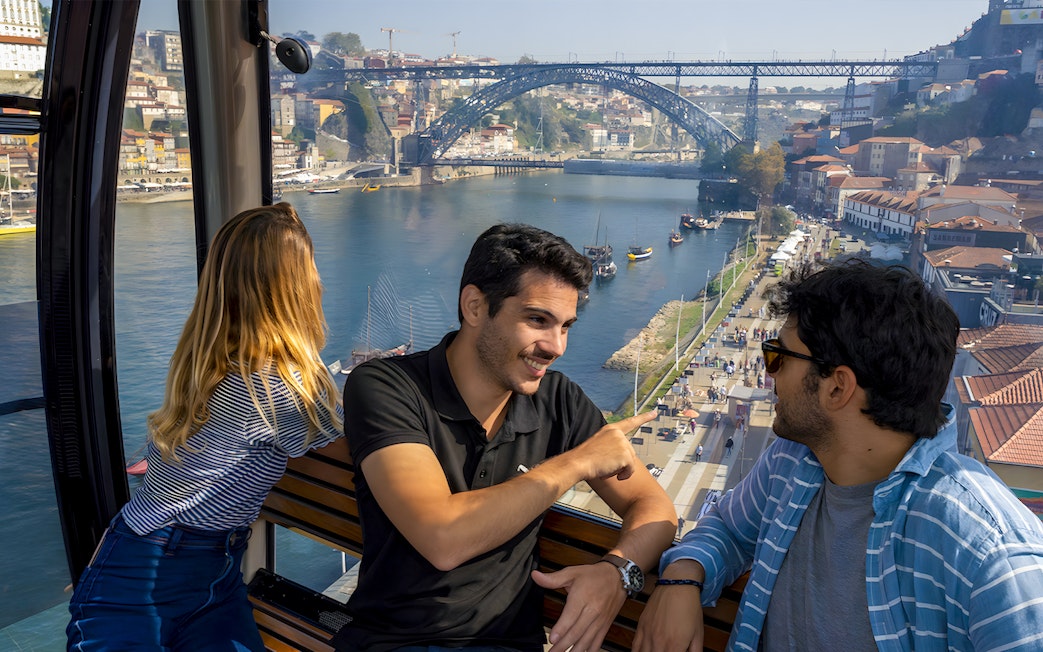 Tourists in cable car with guide overlooking Douro River and Dom Luís I Bridge in Porto.
