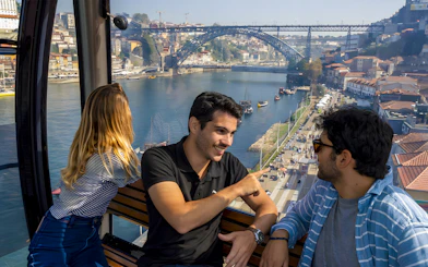 Tourists in cable car with guide overlooking Douro River and Dom Luís I Bridge in Porto.