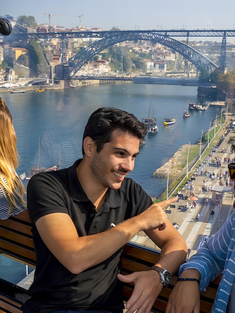 Tourists in cable car with guide overlooking Douro River and Dom Luís I Bridge in Porto.