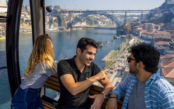 Tourists in cable car with guide overlooking Douro River and Dom Luís I Bridge in Porto.