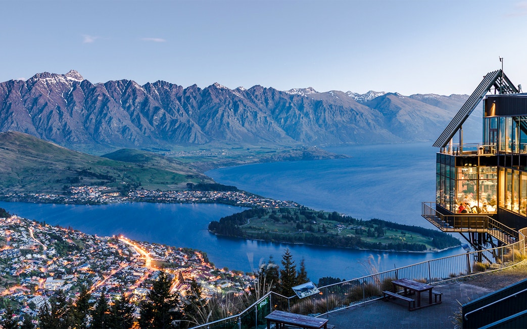 Aerial view of Queenstown with Lake Wakatipu and surrounding mountains at sunset.