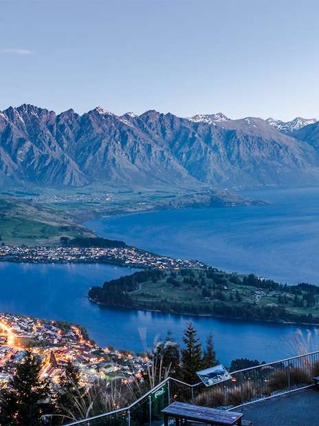 Aerial view of Queenstown with Lake Wakatipu and surrounding mountains at sunset.