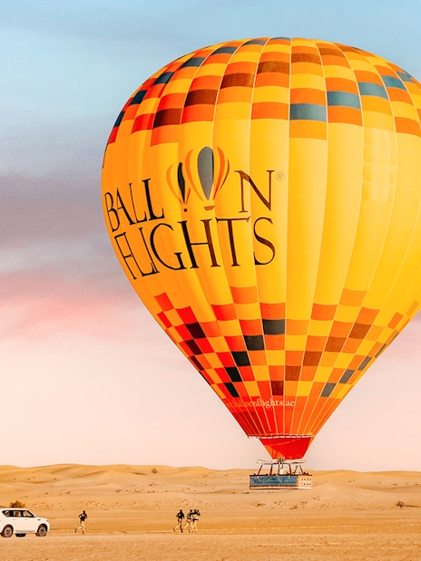 Hot air balloon in desert landscape with vehicles and people preparing for flight.