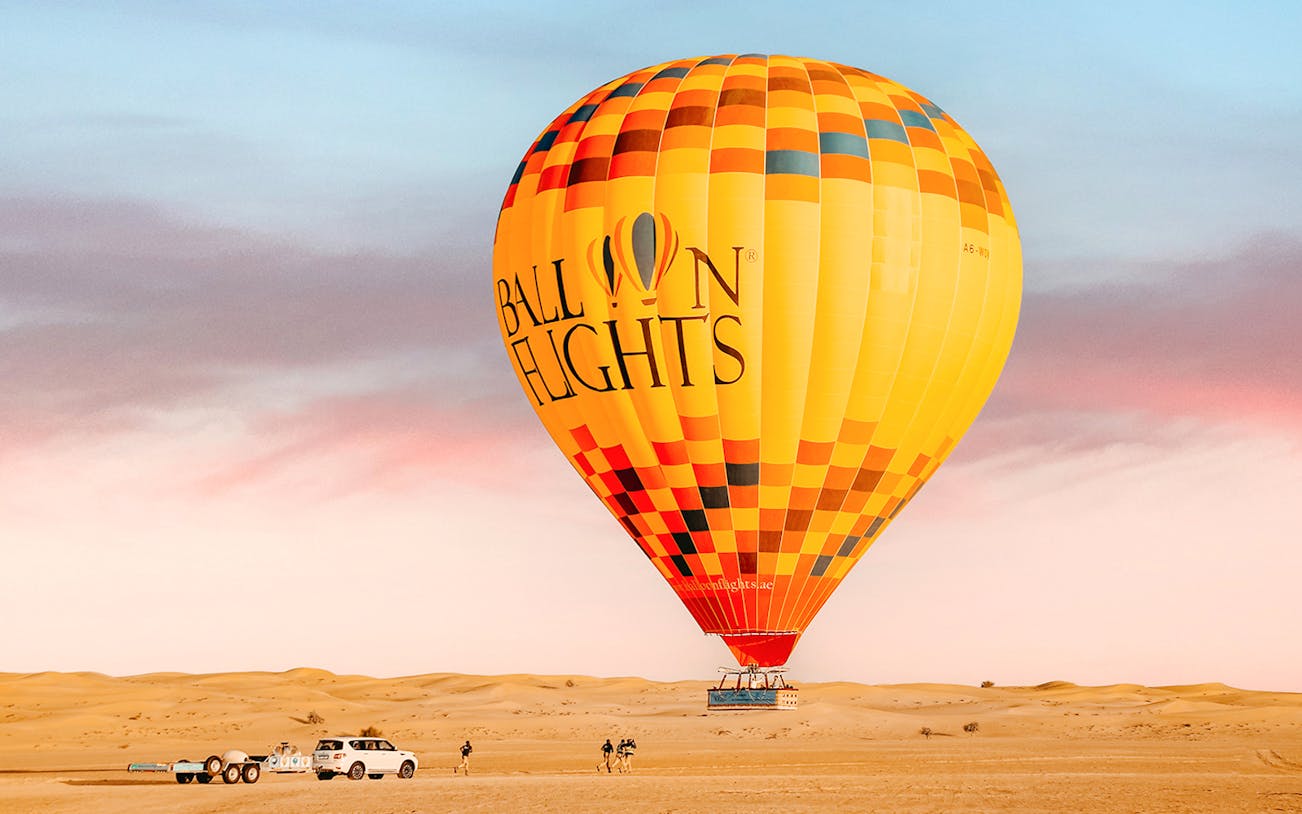 Hot air balloon in desert landscape with vehicles and people preparing for flight.