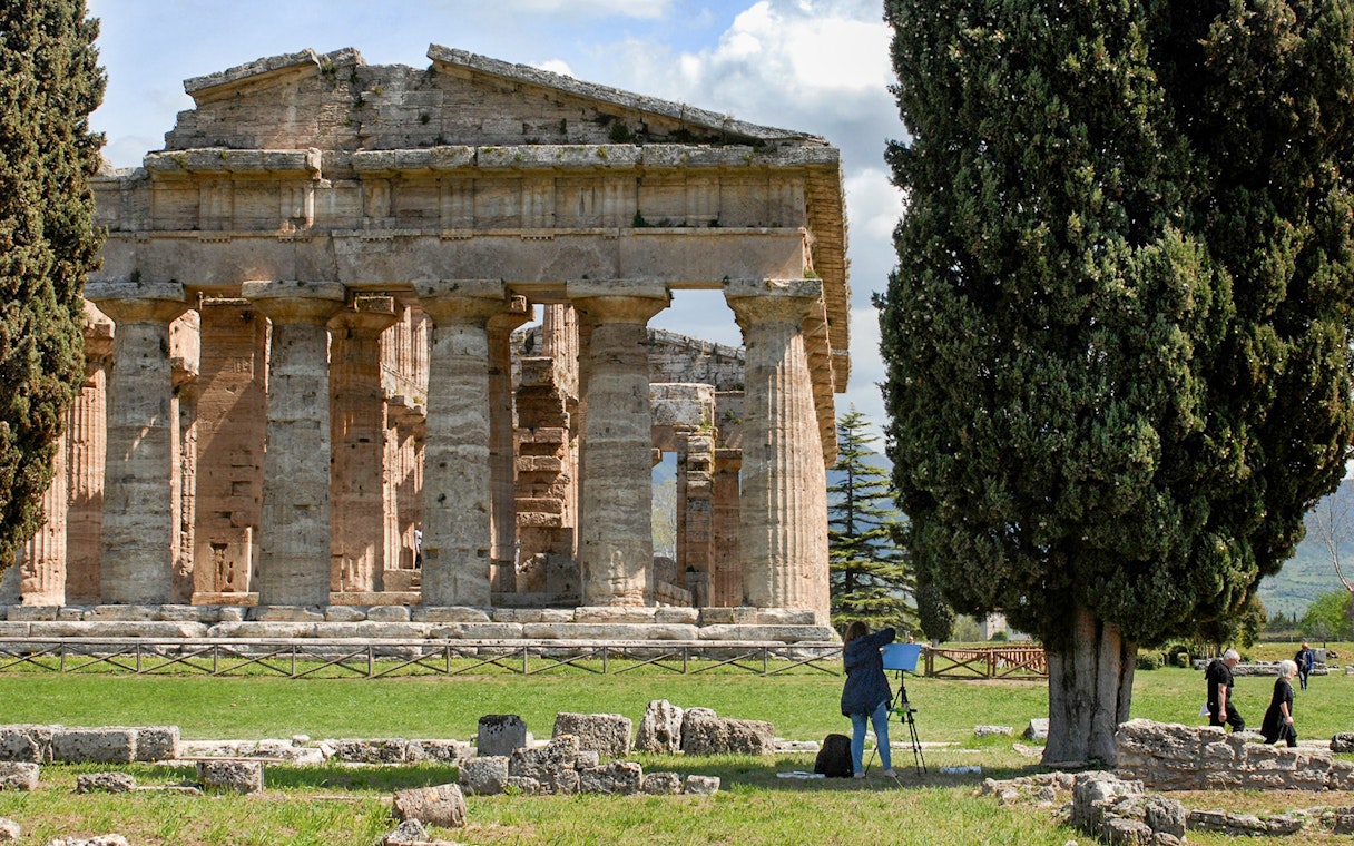 Ancient Greek temple ruins in Paestum, Italy, with tourists exploring the site.