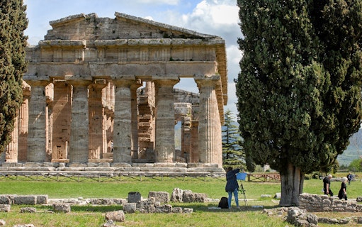 Ancient Greek temple ruins in Paestum, Italy, with tourists exploring the site.