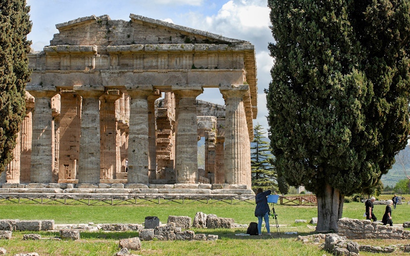 Ancient Greek temple ruins in Paestum, Italy, with tourists exploring the site.