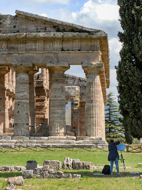 Ancient Greek temple ruins in Paestum, Italy, with tourists exploring the site.