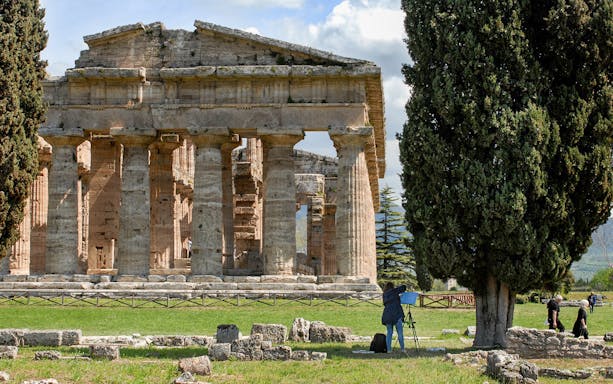 Ancient Greek temple ruins in Paestum, Italy, with tourists exploring the site.