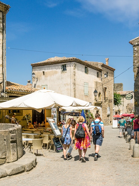 People walking through a historic street in Carcassonne, France, near a stone well and outdoor café.