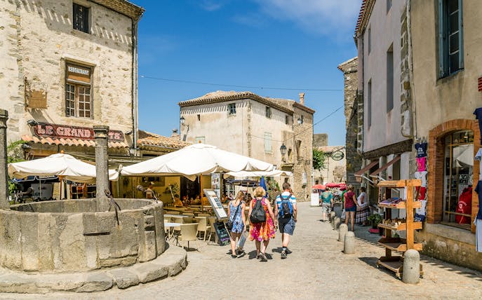 People walking through a historic street in Carcassonne, France, near a stone well and outdoor café.