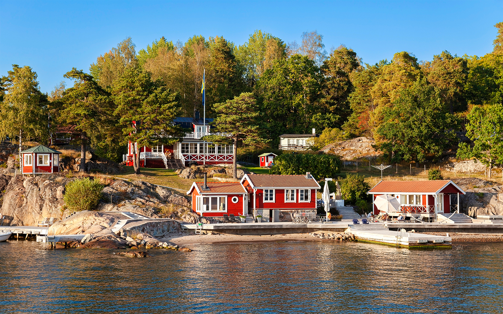 Red cottages on a rocky shore surrounded by trees in the Stockholm archipelago.